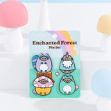 Pusheen Enchanted Forest Pin Set on backing card. The backing card features a forest scene with mushrooms and a wood stump with a purple, pink, and yellow rainbow in the background. 