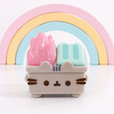 Front view of the Pusheen trash can in front of a pastel-colored rainbow. The small figurine includes Pusheen’s ears extending off the front top of the figure.  