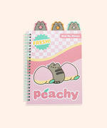 A light pink spiral bound notebook features Pusheen between two pink and yellow peaches. Extending off the top of the colorful peach notebook are three tabs featuring a grey Pusheen the cat holding a strawberry, orange, and watermelon slice. The front of ntoebook features phrases including “fresh!” “best by: always,” and “peachy.”