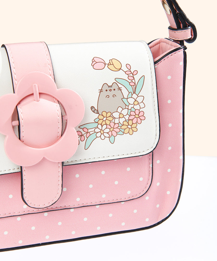 Close-up view of the Pusheen with flowers graphic on the closure flap of the Pusheen Springtime Purse. Pusheen stands in a flower bed with tulips, daisies, and green leaves.