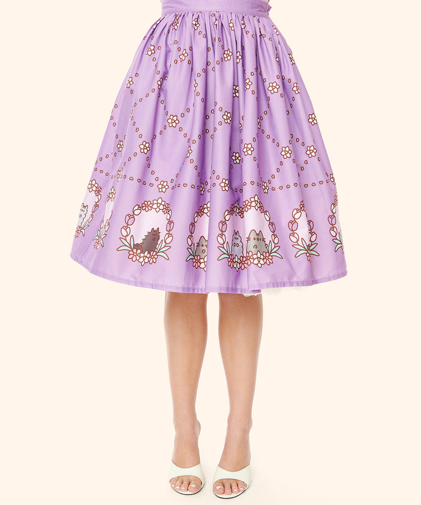 Closeup view of the printed pattern on the Pusheen Springtime Skirt. Pusheen, Stormy, and Pip are posed in a portrait surrounded by tulips and other flowers in a frame. Above the hem print is a diamond pattern made up of tiny hearts and six-petal flowers.