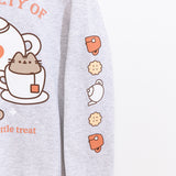Close-up view of icons printed on the wearer’s left sleeve of the grey sweatshirt. The icons include a salmon teacup, yellow biscuits, and a white tea kettle. 