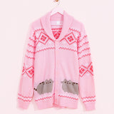 Pink knit cardigan hangs on a pink hanger in front of a light pink wall. The unisex cardigan features Pusheen the Cat in grey and brown surrounded by dark pink diamond pattern and white hearts and diamond pattern all over the sleeves and top of button up cardigan. 
