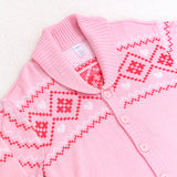 Close-up view of the diamond and heart print at the top of the cardigan. The cardigan has fold over lapels that match the ribbed hem and cuffs. The pattern features a variety of diamonds, hearts, and squiggles.  