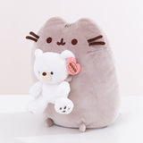 Quarter side view of the Pusheen x GUND plush. The sitting cat holds a small white bear with black eyes and embroidered paw pads.