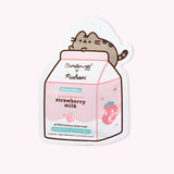Front view of the individual sheet mask packaging. Pusheen the Cat waves atop a strawberry milk container. The carton shows product details including that the product includes strawberry, lactic acid, and vegan collagen.
