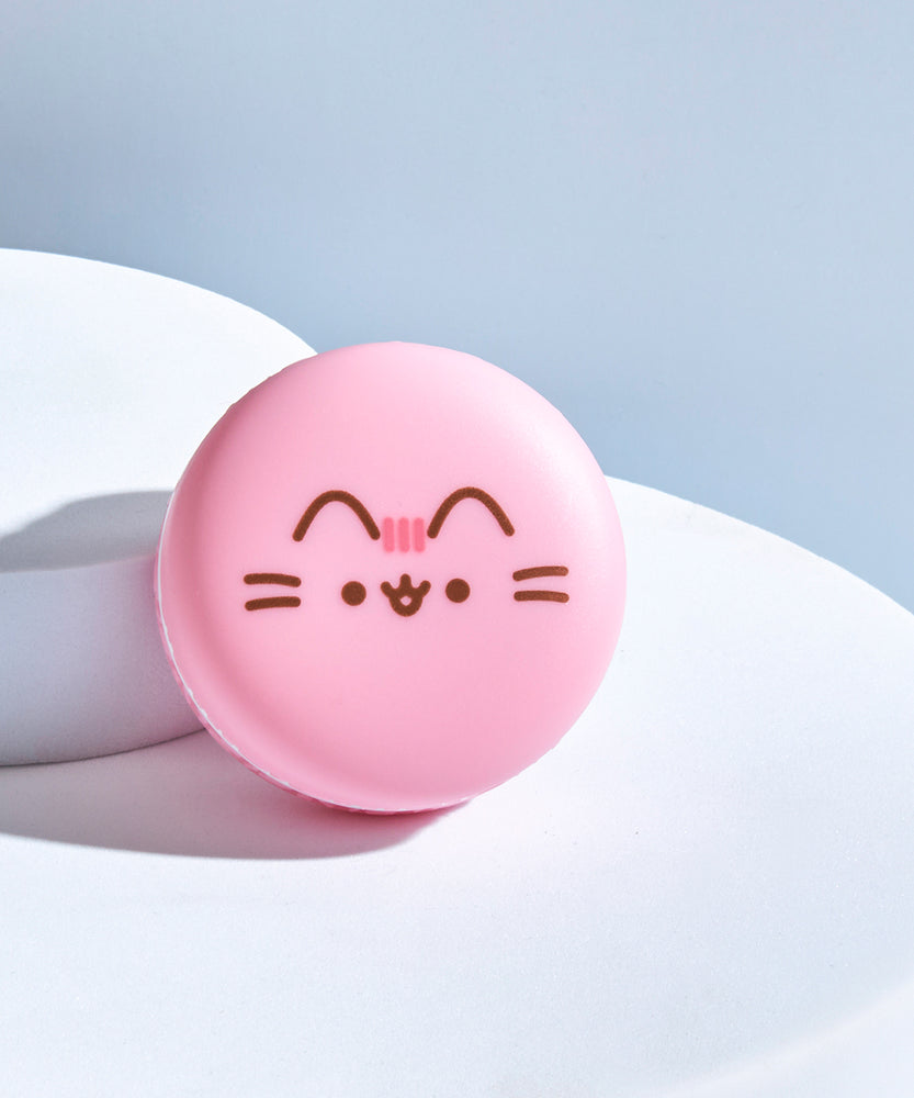 Front view of the Pusheen Strawberry Macaron Lip Balm. The circular component has Pusheen's ears, head stripes, eyes, mouth and whiskers printed in brown and pink on the front.