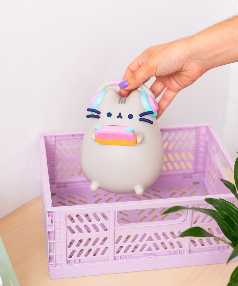Model holding Pusheen Gaming Lamp to show size of lamp. The grey, light pink, light blue, and orange lamp is held above a purple basket.  