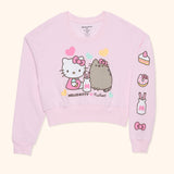 Front view of ladies cropped sweatshirt with the left sleeve folded to reveal the sleeve design that starts at the shoulder and finishes at the shoulder cuff.  up of the right side of the tee. A slice of cake, a donut, a milk bottle, and Hello Kitty's bow is are screen printed onto the light pink sweatshirt.