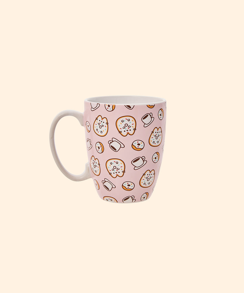 Front view of the Pusheen Pink Donuts & Coffee Mug. The light pink mug has a white handle and interior walls. The outside of the mug features a repeating pattern of Pusheen the Cat as a glazed donut with rainbow sprinkles surrounded by coffee cups and rainbow glazed donuts.