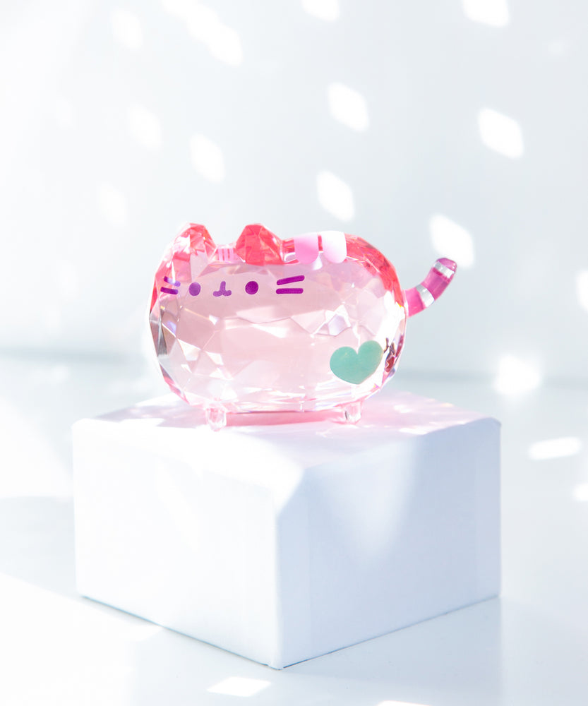 Light reflecting off the Pusheen Facets that sits atop a white box. In the background, reflective lights can be seen shining off the Facets.  