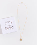 Full view of the gold charm necklace on top of a white background, the square jewelry box lid besides it.