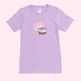 A light purple graphic short sleeve tee against a light pink background. The graphic in the center of the t-shirt features Pusheen as an ice cream cake accompanied by a pink and white heart with the phrase ‘Chill’ inside. 