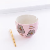 The Pusheen Ramen Bowl with the pair of chopsticks resting on the ground to the left, in front of a white background.