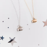 Gold and Silver charm necklaces next to one another on top of a white blanket and surrounded by silver stars. The charm features Pusheen sitting in a loaf pose, with her feet tucked in and her tail by her side. 