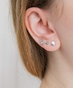 Closeup of a model’s ear wearing the Silver Pusheen Charm Stud Earrings on their lobe, along with their two other piercings that are wearing different silver stud earrings. The Pusheen Stud earring is bigger then a simple dot earring.