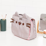 Quarter front view of Pusheen Toiletry Bag. The grey polyester bag features Pusheen the Cat with accompanying grey ears, stripes, and brown facial embroidery. The bag has a top handle for carrying.  
