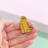 Model’s hand holding the sloth pin in front of a mint and pink background. The pin is small, only slightly taller then the width of two fingers.