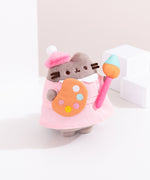  Right quarter view of the Artist Plush. Pusheen's pudgy paws hold a paint-filled palette and used plush paintbrush.