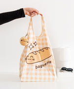Model holds yellow gingham bag handle with Pusheen the Cat as a baguette bread graphic.