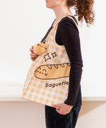 Model holds nylon bag on shoulder while showing off the attached baguette plush near the handle.