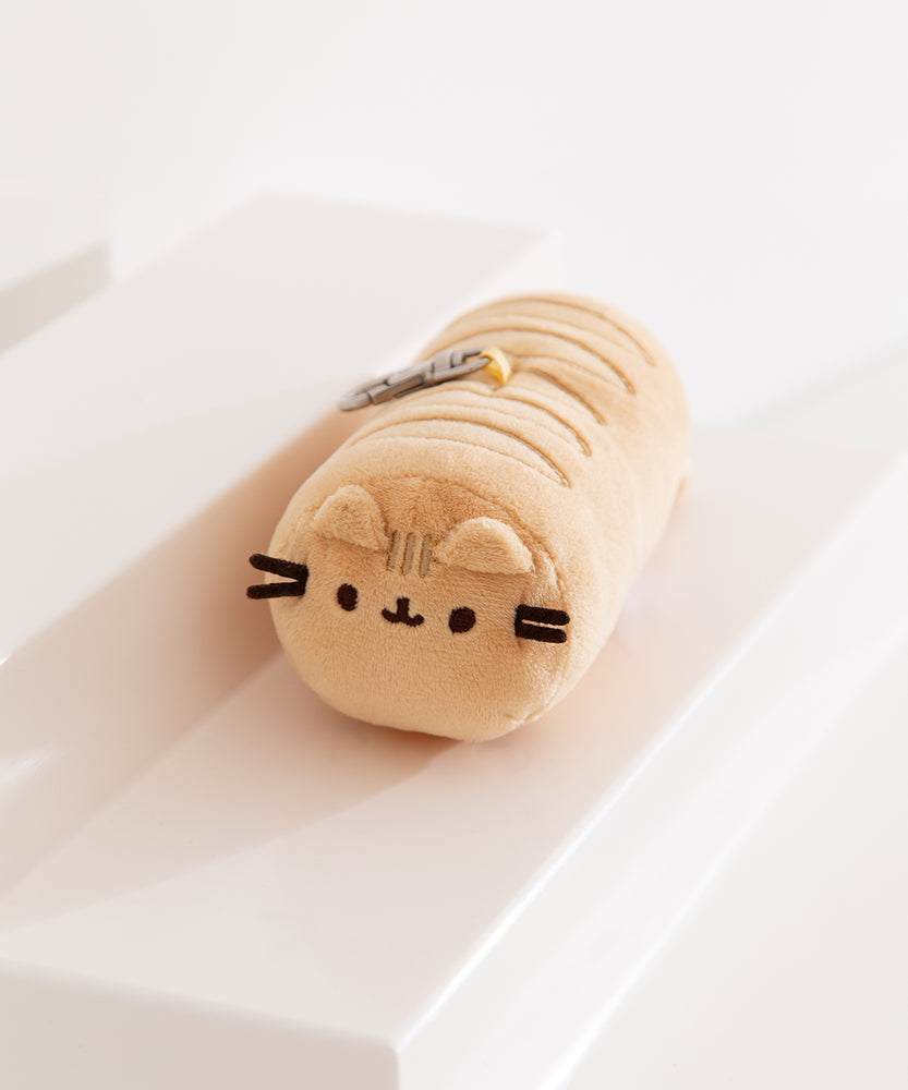 Left side view of yellow keychain plush. The front of the round bag has Pusheen the Cat's face embroidered on as well as two plush cat ears.