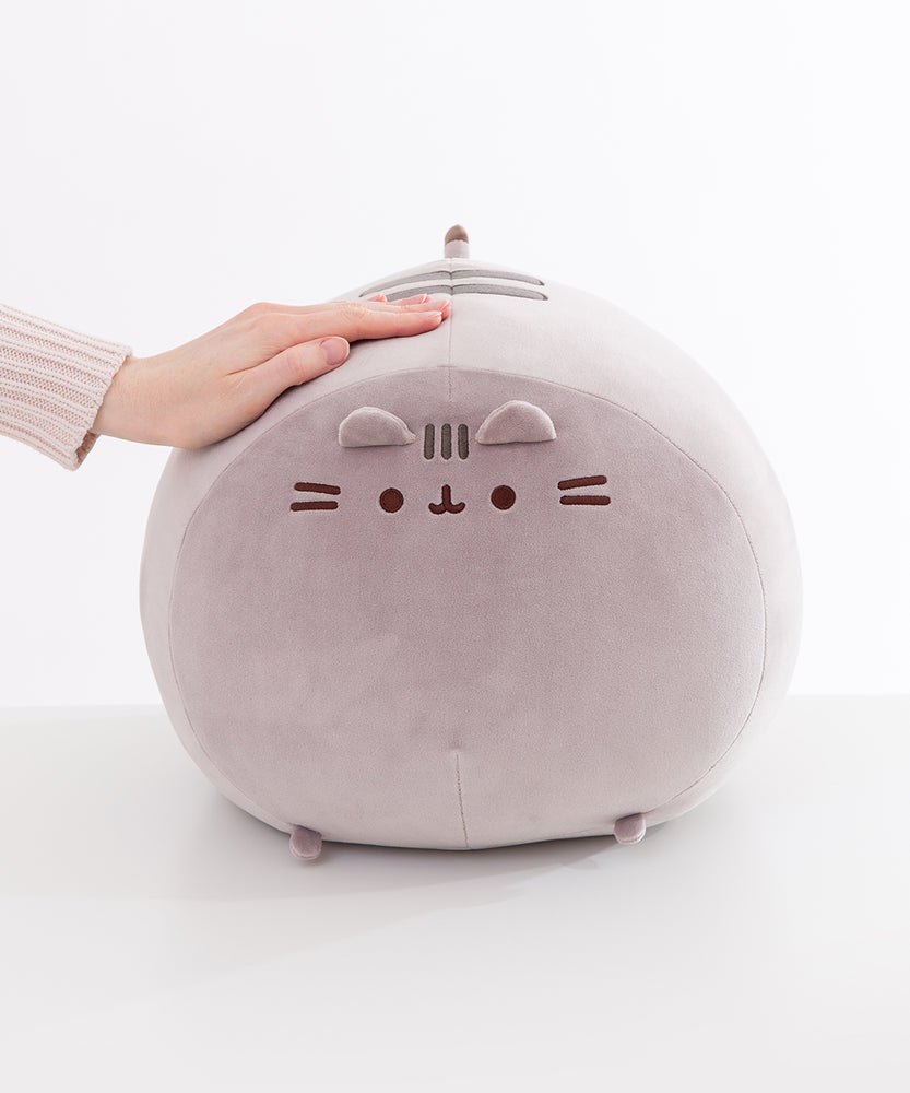 Jumbo squisheen sits on a white surface A hand rests atop the oversized circular plush.