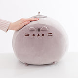 Jumbo squisheen sits on a white surface A hand rests atop the oversized circular plush.