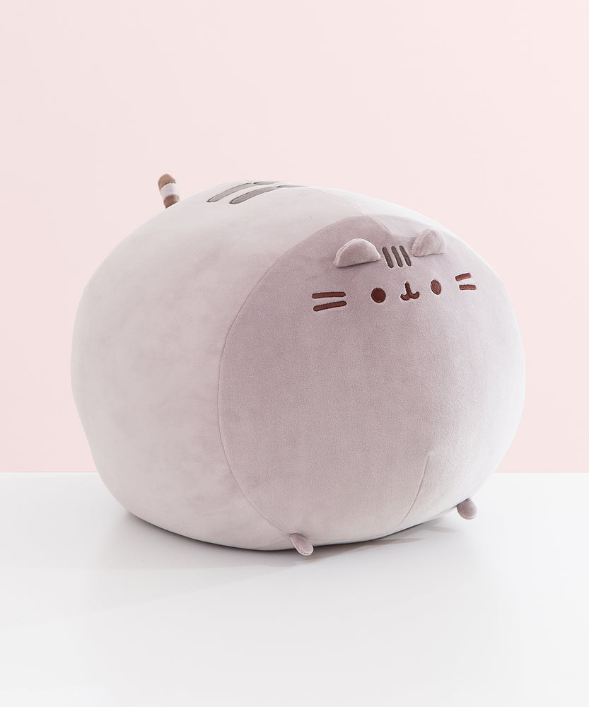 Side view of the front of the extra large squisheen plush of Pusheen. The rounded grey plush has two triangle shaped ears that extend off the top front of the plush.