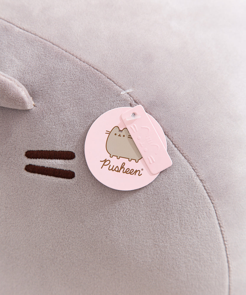 Close-up view of the Pusheen logo and Pusheen label pink tags that are affixed near the front face of the jumbo grey plush.