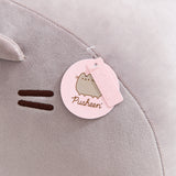 Close-up view of the Pusheen logo and Pusheen label pink tags that are affixed near the front face of the jumbo grey plush.