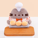 Close-up of Pusheen holds three biscuit buns on a grey slab on a wood countertop. Pusheen wears a white patisserie chef’s hat between her two fuzzy gray ears. Image includes the text "*countertop not included" in top left corner of image.