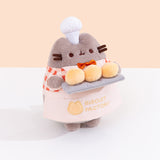 Other side quarter side view of Baker Plush. Pusheen the Cat holds three biscuit buns on a light gray platter. 