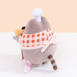 Back quarter view of plush. Pusheen wearing a baking apron stands upright on two pudgy paws. 