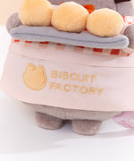 Close-up view of the apron Pusheen wears that says, “Biscuit Factory” accompanied by a cat outline logo. 