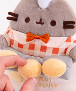 Close-up view of the light-yellow buns that Pusheen holds. Model holds one biscuit to show that the buns are attached to the plush. 