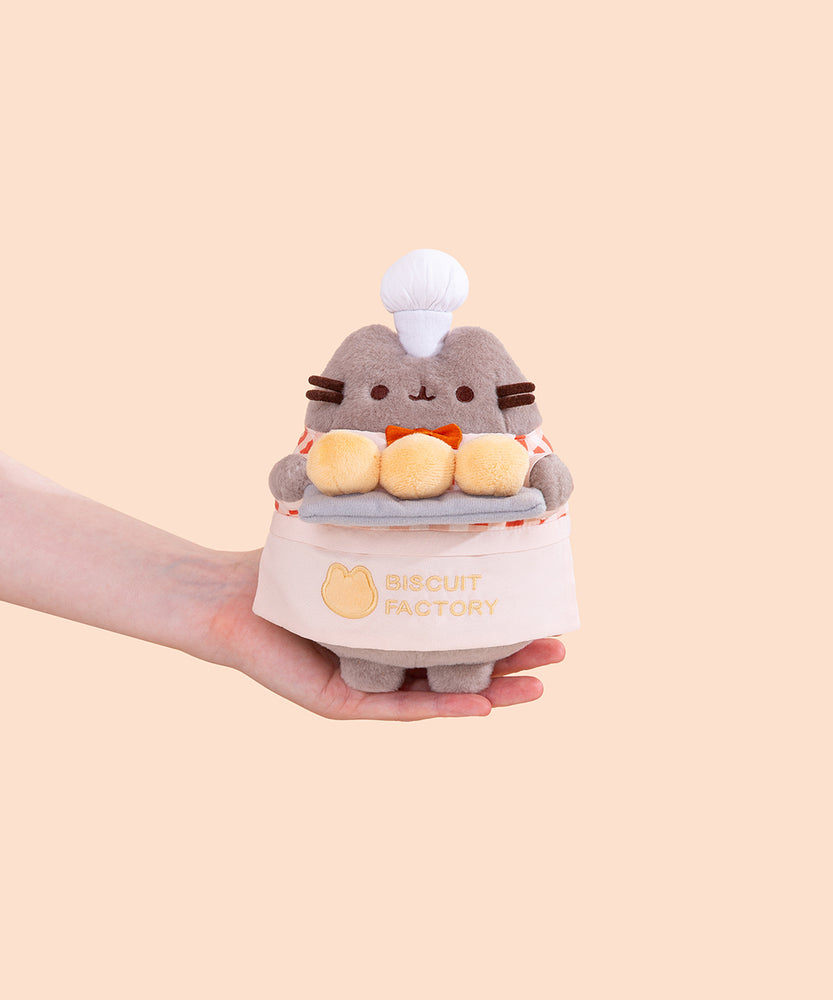 Model holding Biscuit Baker Pusheen Plush to show size scale. The bottom of the grey fashion Pusheen plush fits in the model’s palm. 