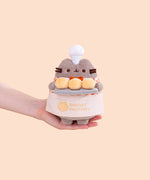 Model holding Biscuit Baker Pusheen Plush to show size scale. The bottom of the grey fashion Pusheen plush fits in the model’s palm. 