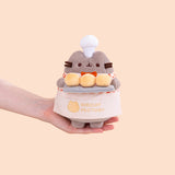 Model holding Biscuit Baker Pusheen Plush to show size scale. The bottom of the grey fashion Pusheen plush fits in the model’s palm. 