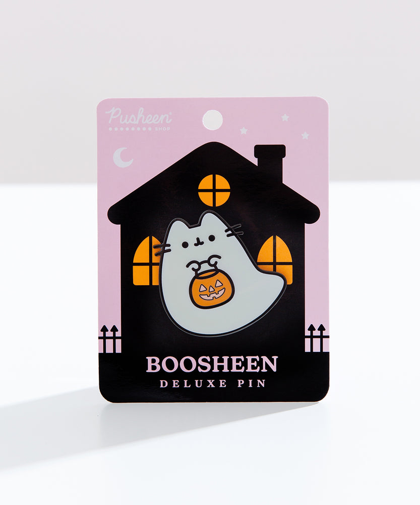 Boosheen Pusheen Deluxe Pin attached to backer card. The ghost shaped pin sits on a white surface and depicts Pusheen the Cat as a friendly ghost while carrying a jack-o'-lantern candy pail. 