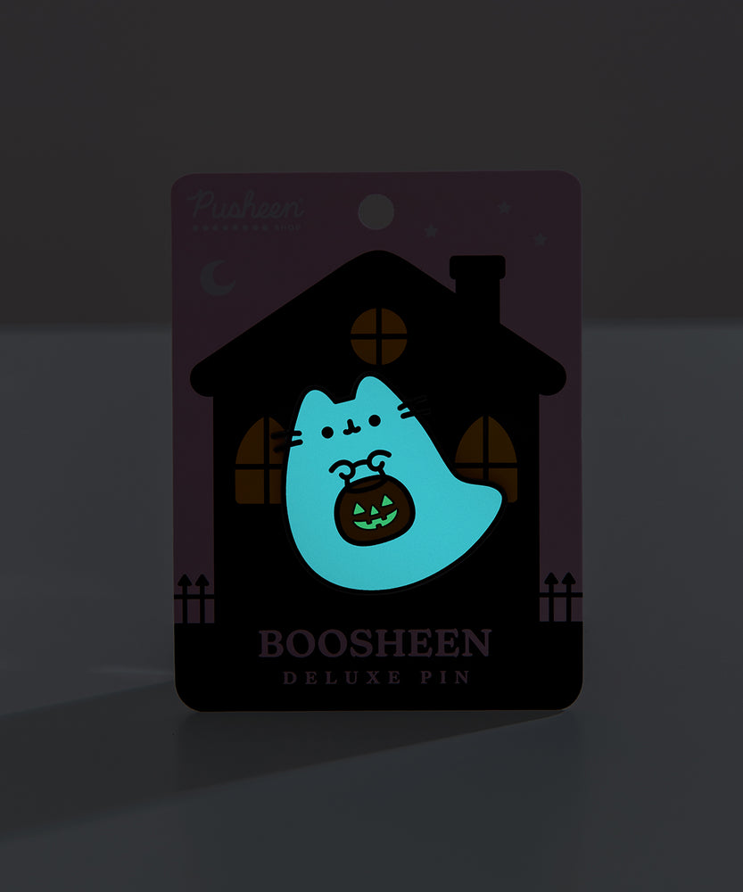 Front view of the glow in the dark element of the Halloween-themed Pusheen pin. The ghost glows light blue while the pumpkin candy pail glow slight green in the dark after being exposed to light.   