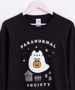 Close-up view of large front graphic on the center of the Boosheen Halloween Pusheen long-sleeve tee. Above and below the ghost and spooky scene are the words “Paranormal Society” printed in white. 