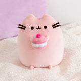 Front view of the Pusheen Sweets Cherry Macaron Squisheen Plush. Pusheen the Cat is shown in light pink holding a pink macaron topped with a bright pink cherry and fluffy white filling.