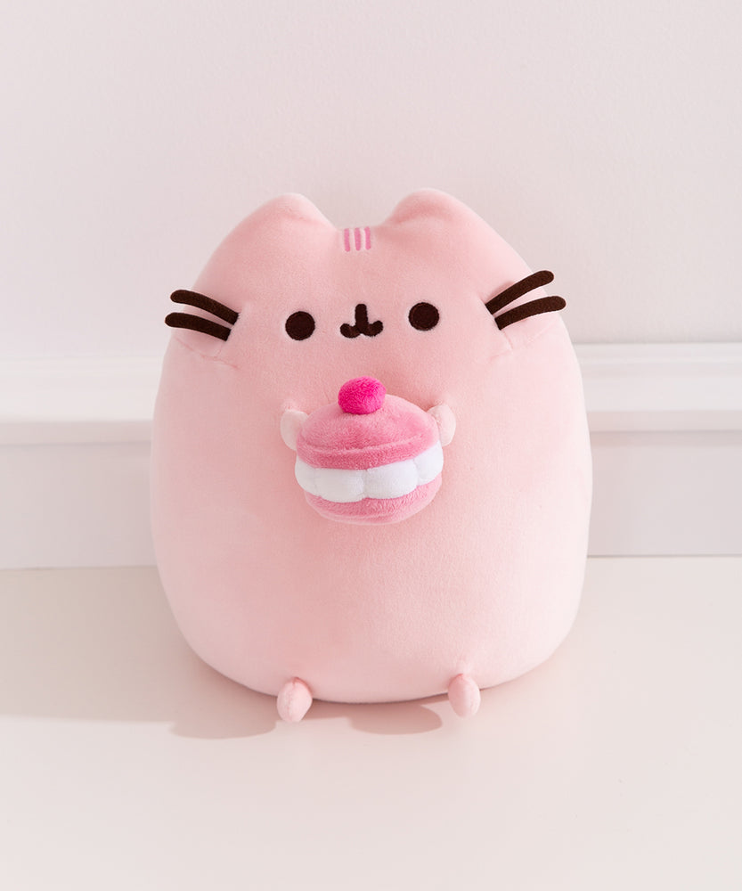 Front view of the Pusheen Sweets Cherry Macaron Plush. The light pink cat plush features dark pink stripe details between her two ears.