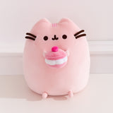 Front view of the Pusheen Sweets Cherry Macaron Plush. The light pink cat plush features dark pink stripe details between her two ears.