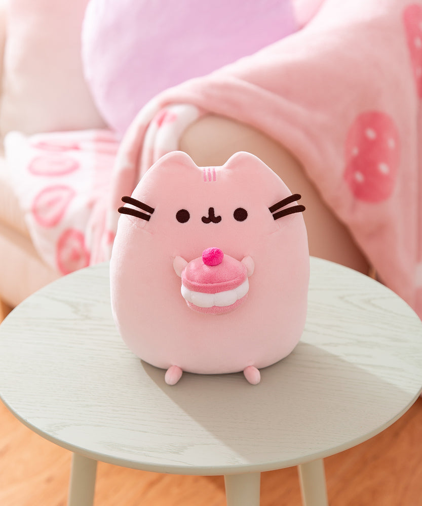 Front view of the Cherry Macaron Squisheen. The pink plush shows Pusheen the cat holding a multi-pink cherry macaron in her front paws.