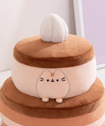 Side quarter view of the chocolate cake Pusheen plush. The cake plush has a light brown cake layer in the top and at the bottom of the bottom section. 