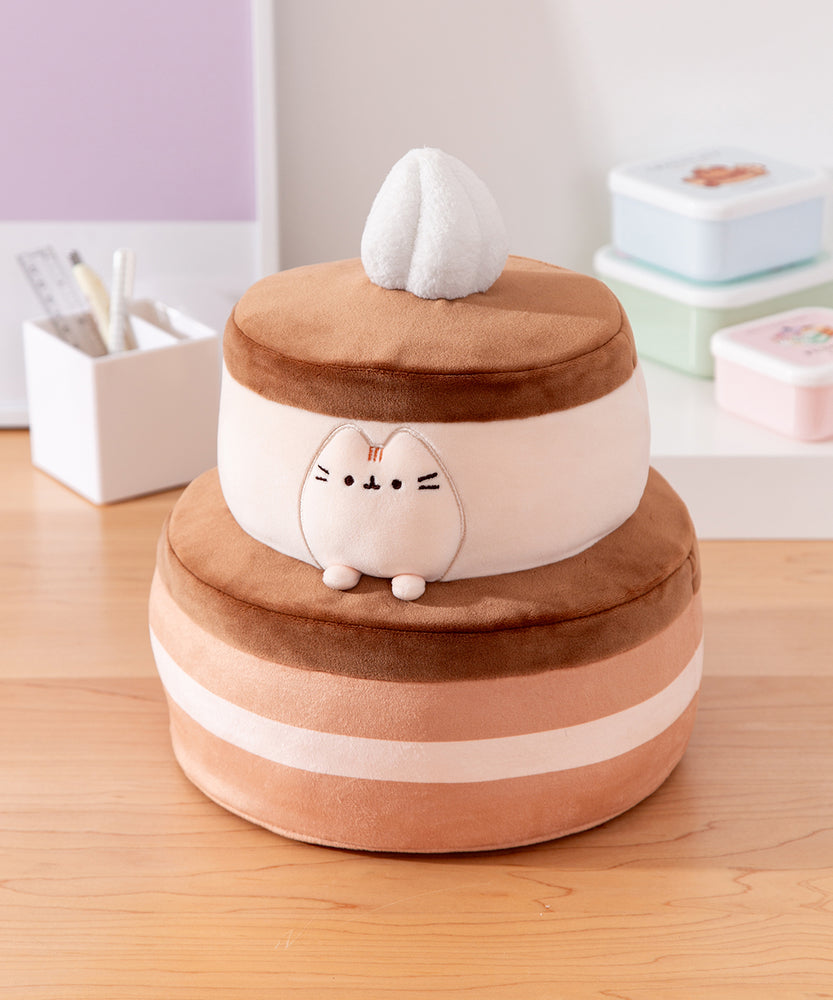 Cake Squisheen shown on a desktop to show scale of 11" tall plush toy. Pusheen the Cat rests inside the top tier of the cake plush.