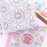 Interior page view of the Pusheen coloring book. A graphic of Pusheen lying in the center of a flower is partially colored using colored pencils that are laid out to the side of the coloring book. Below the interior page of the activity book is another copy of the book showing the pastel-colored front cover. Next to the books are paper clips, a pencil sharpener, an eraser, and three colored pencils. 