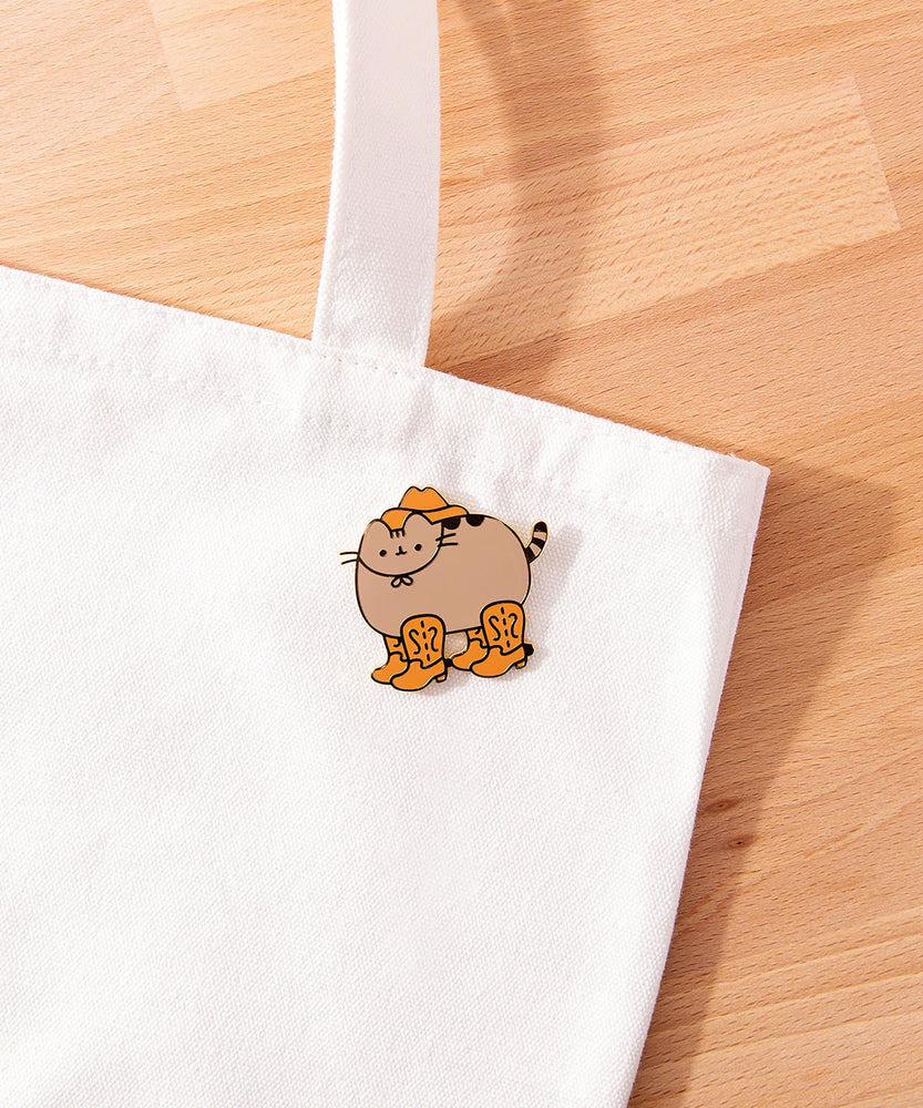 Cowboy Boots Pusheen Pin attached to a white tote bag to show the brown and gray colors on the pin.